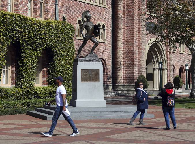 FILE - People pose for photos, March 12, 2019, in front of the iconic Tommy Trojan statue on the campus of the University of Southern California in Los Angeles. As more than 2 million graduating high school students from across the United States finalize their decisions on what college to attend this fall, many are facing jaw-dropping costs — in some cases, as much as $95,000. (AP Photo/Reed Saxon, File)