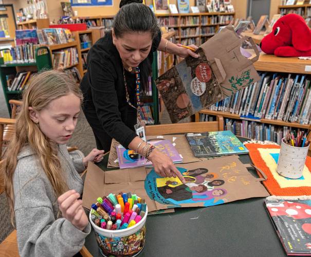 Molly Valentine, a Crocker Farm Elementary student, works with librarian and teacher Waleska Santiago-Centeno on panels for the Memory Project. For the project, students created hanging banners featuring women from picture books they have read in the library.