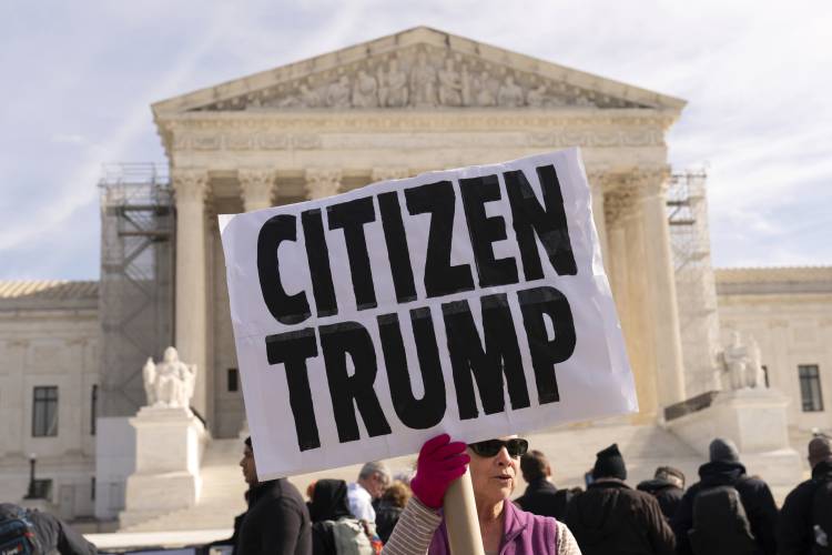 A demonstrator holds a banner outside of the U.S. Supreme Court, Thursday, Feb. 8, 2024, in Washington. The U.S. Supreme Court on Thursday will take up a historic case that could decide whether Donald Trump is ineligible for the 2024 ballot under Section 3 of the 14th Amendment. (AP Photo/Jose Luis Magana)