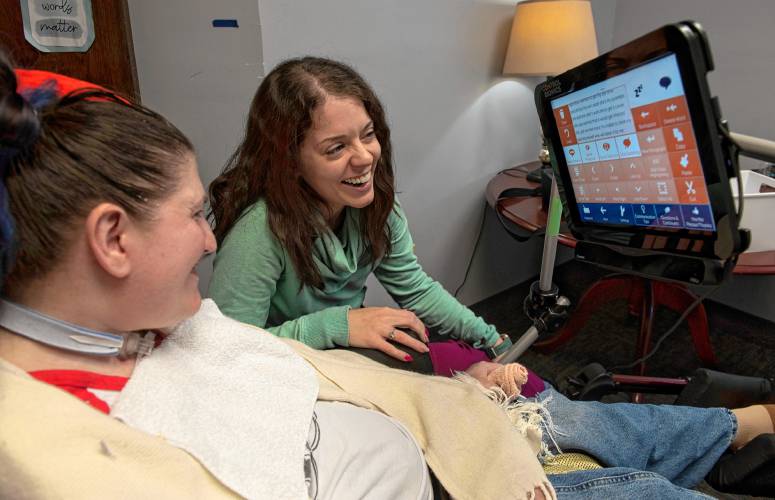 Megan Golightly, a speech-language pathologist at Strive Clinic in Holyoke, laughs with Mel Hearne while listening to the computer read what Hearne wrote about how she spent her weekend. Hearne is learning how to use an Eye Gaze Trilogy which allows Hearne to communicate by using her eyes to select symbols and letters.