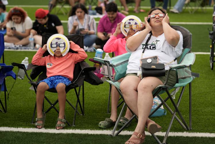 Karine Rodriquez, right, sits with her son Yurem, left, and daughter Aranza, center, as the moon partially covers the sun during a total solar eclipse, as seen from Eagle Pass, Texas, Monday, April 8, 2024. (AP Photo/Eric Gay)