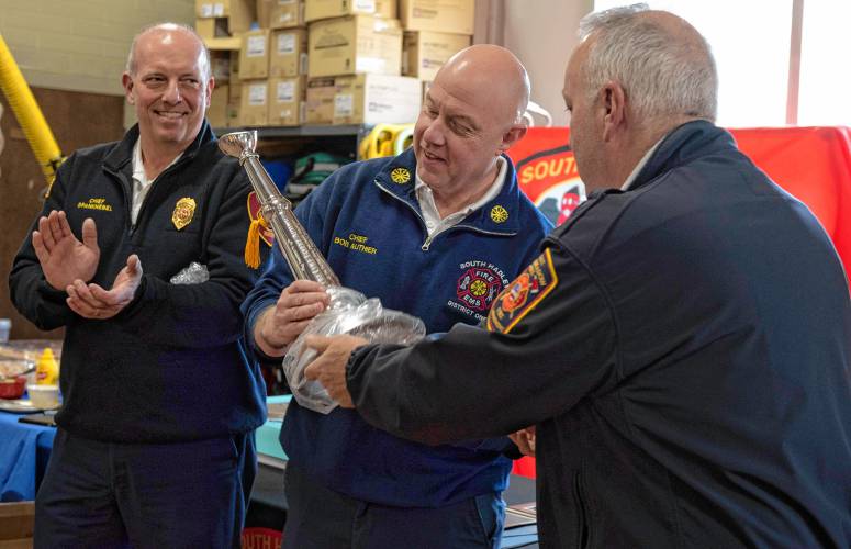 Robert Authier, the retiring fire chief of South Hadley’s Fire District 1, receives a silver bugle from Paul Morrissette, East Longmeadow fire chief, while Michael Spanknebel, left, Hadley’s fire chief, watches during Authier’s retirement celebration at the South Hadley station Friday.
