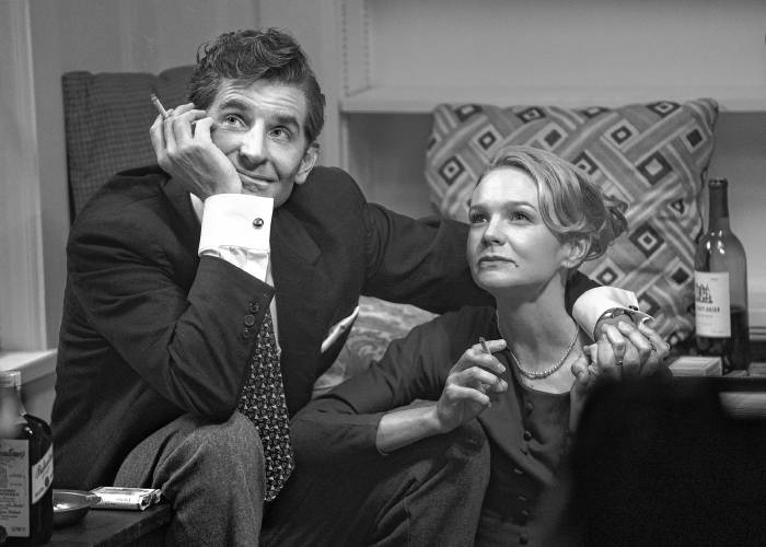 Bradley Cooper as Leonard Bernstein, and Carey Mulligan as his wife, Felicia Montealegre, smoke and cuddle in a scene from “Maestro.”