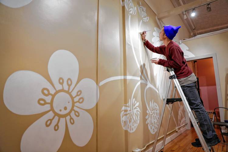 Small Victories owner Isa Wang works on a mural painting on the store walls last Thursday afternoon ahead of the retail shop’s grand opening on this coming Friday inside Thornes Marketplace in Northampton. The shop will offer a variety of handmade wares from greeting cards that can be planted to grow herbs or wildflowers, along with pins for easy identification of a person’s pronouns.