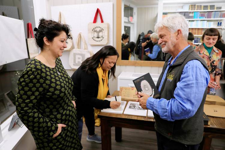 Authors Ani Gjika, left, and Grace Talusan sign copies of their award-winning Restless Book titles for Dean Cycon of Leverett during the recent opening celebration of Restless Books in Amherst. Gjika is the author of “An Unruled Body” and Talusan of “The Body Papers.”