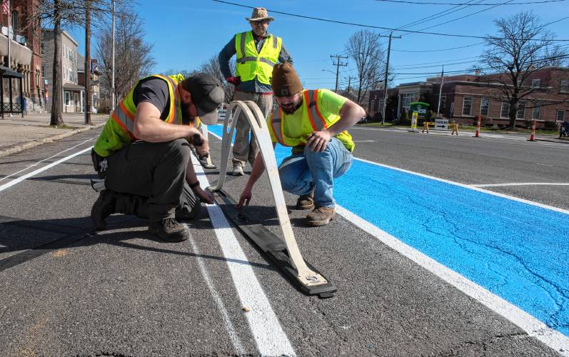 Easthampton Highway Department employees Tom Cormier, left, and Andrew Bishop, right, set up a barrier as part of the experimental Easthampton Main Street redesign while Andrew Howard, owner of Team Better Block, watches. The barrier is between the bike lane and handicap parking. 