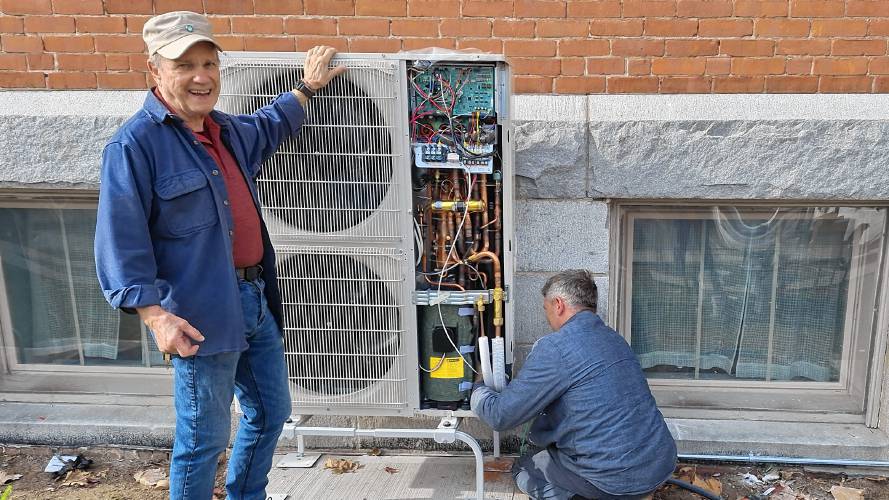 John Poirier, left, a member of the Unitarian Society of Northampton and Florence who serves on the society's House and Property Committee, stands with one of the new heat pumps installed in order for the church to meet its decarbonization goals. 