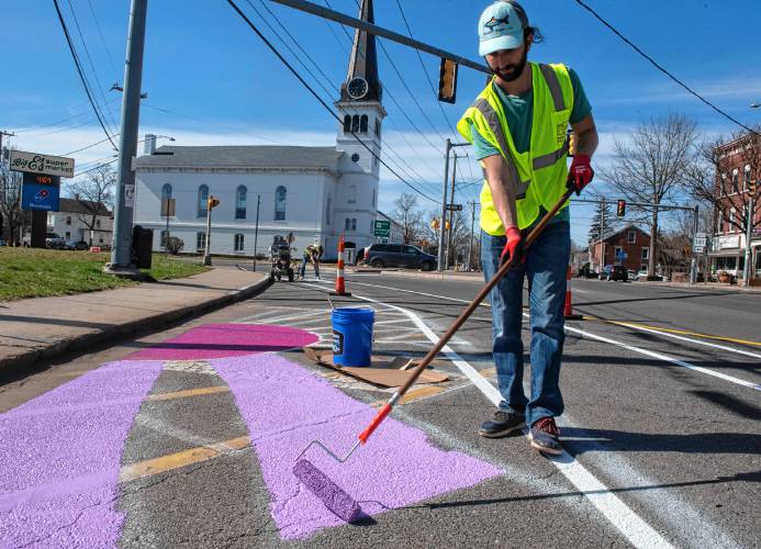Jake Morris, an employee of Team Better Block, paints a mural on the pedestrian portion of the Easthampton Main street experimental redesign. Next to Morris is a designated bike lane. 