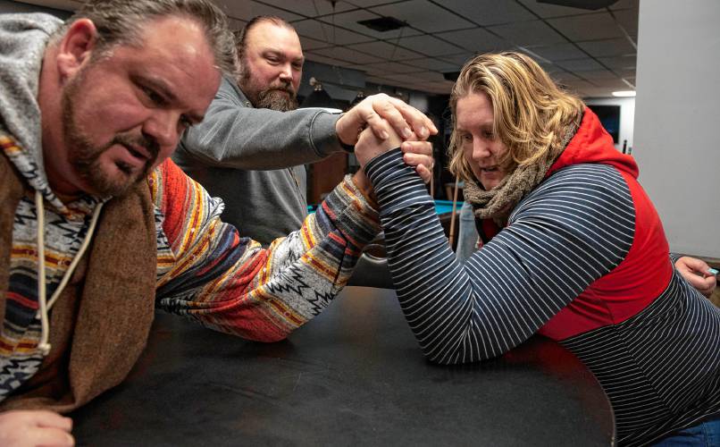 Donald Carberry, a co-sponsor for the arm wrestling event The Pulaski Pull Down, and Rose Lynch demonstrates a practice session while Chris Parker, middle, sets them up, at Se7ens Sports Bar and Grill in Easthampton on Dec. 6.