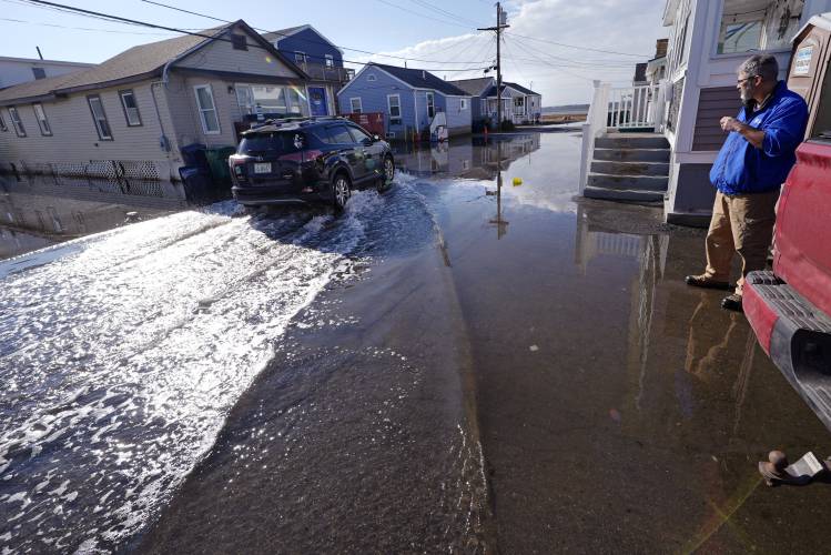 Haim Levy watches as a neighbor drives through high tide waters, covering the road with sea water, at his cottage near Hampton Beach, which was flood damaged during January 2024 storms, Friday, Feb. 9, 2024, in Hampton, N.H.