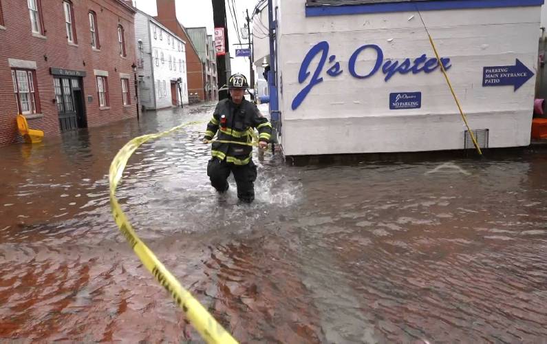 Wind whips caution tape as a firefighter closes off a flooded waterfront street during a severe storm in this Jan. 10, 2024, in Portland, Maine.