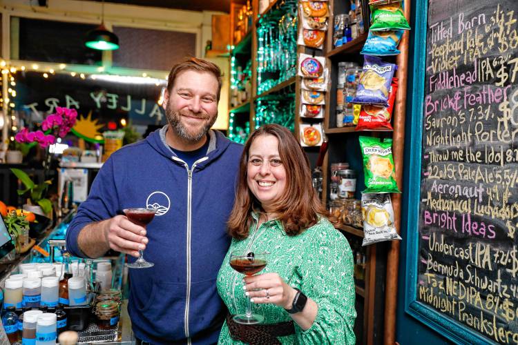 Owners Ed and Juliette Mooers pose for a photo with a pair of cocktails behind the bar at Valley Art Supplies on Cottage Street in Easthampton.