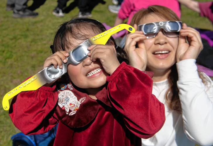 Josie Liang and her mother Xu Chen use protective glasses to look at the eclipse at the UMass Sunwheel on Monday. 