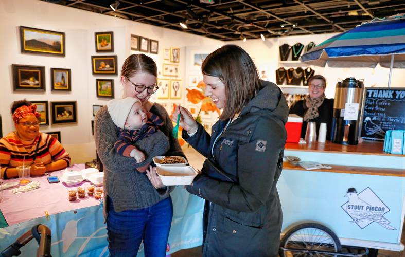 Meagan Mitchell, right, tries a bite of apple crumb pie as her 5-month-old Finnian looks on with Nicole Allen during a pop-up Pi Day event with Carefree Cakery and Stout Pigeon Coffee on Thursday at the Mill District General Store and Local Art Gallery in Amherst.STAFF PHOTOS/DAN LITTLE
