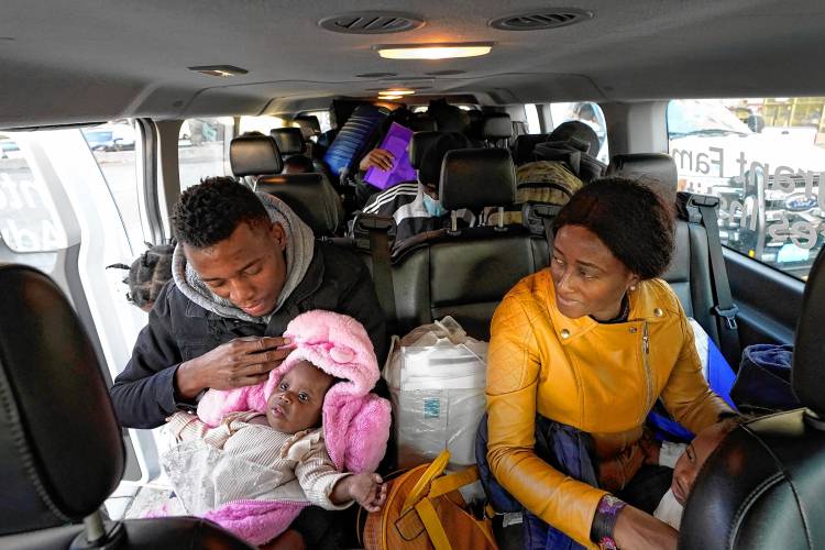 Petterly Jean-Baptiste holds a child as he and his wife, Leonne Ysnardin, both immigrants from Haiti, load into a van in Boston to await transportation to a shelter in Quincy in November.