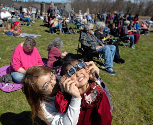 Xu Chen helps her daughter, Josie Liang, use glasses to look at the eclipse at the UMass Sunwheel on Monday afternoon. 