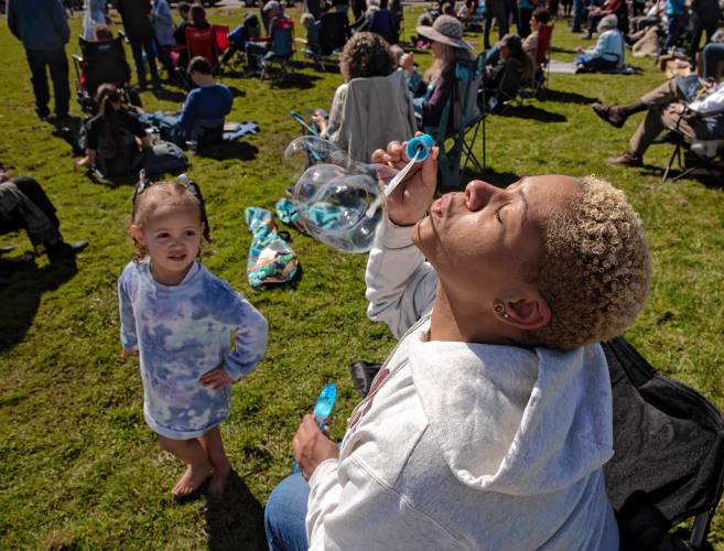 Ariana Sims-Butler blows bubbles for her daughter, Anaira Sims-Butler, during the eclipse at the UMass Sunwheel on Monday afternoon. Hundreds of spectators took in the partial eclipse on the UMass campus.