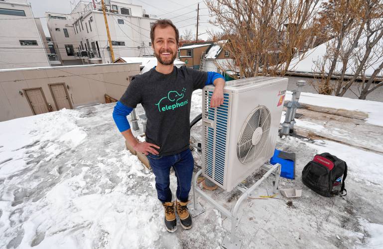 David Richardson, co-founder of Elephant Energy, leans on a condenser placed on the roof during the installation of a heat pump in an 80-year-old rowhouse last January in northwest Denver.