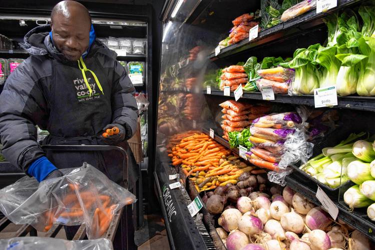 Basil Celestin, an employee at River Valley Co-op, stocks vegetables from Winter Moon Roots in Hadley.