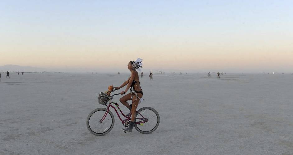 A woman rides a bicycle on the playa after sunset at the Burning Man festival in Gerlach, Nev., Friday, Aug. 30, 2013. Burning Man organizers don’t foresee major changes in 2024 thanks to a hard-won passing grade for cleaning up this year’s festival. Despite the successful inspection, debate continues over whether the 30-year-old gathering has grown too big. Some question whether it has veered too far from its core principles of radical inclusion and participation.