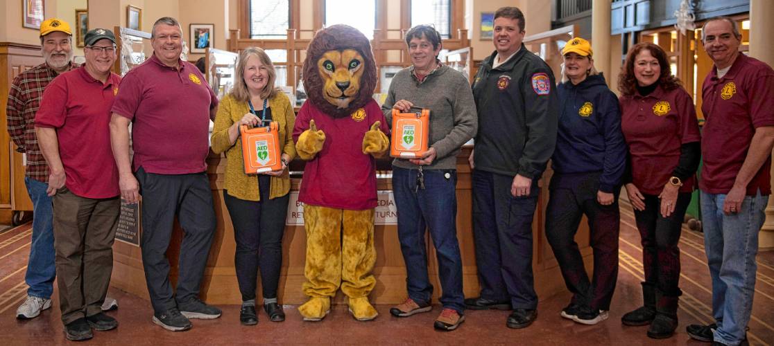 The Northampton Lions Club donated new automated external defibrillators on Wednesday to Forbes and Lilly libraries. From left are Lions Club members Phil Giers, Mark Moggio and Patrick Diggins, Forbes Library Director  Lisa Downing, Lions Club member Isabelle Richards as the mascot, Lilly Library Director Adam Novitt, Northampton Fire Department Assistant Chief Matt Lemberg, and Lions Club members Eileen Young, Kathy Curtis and Steve Richards.