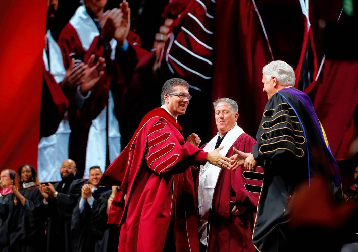 UMass Amherst Chancellor Javier Reyes, left, shakes hands with UMass President Marty Meehan during his inauguration as the 31st leader of the University of Massachusetts on Friday at the Mullins Center in Amherst as board of trustees chair Stephen Karam watches.