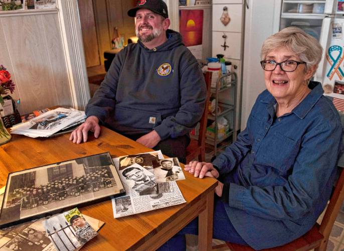 Brendan and Cheryl Quinn sit with photographs of Brendan's great uncle and his mother Cheryl's uncle, Merle Chester Joseph Hillman. 