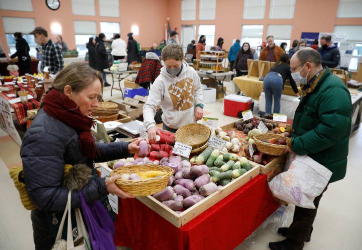 Amanda Groblewski, center, assists Heidi Scott, left, and Mark Rosenberg as they shop for produce from Winter Moon Roots during the Grow Food Northampton Winter Market in January 2023 at the Northampton Senior Center.