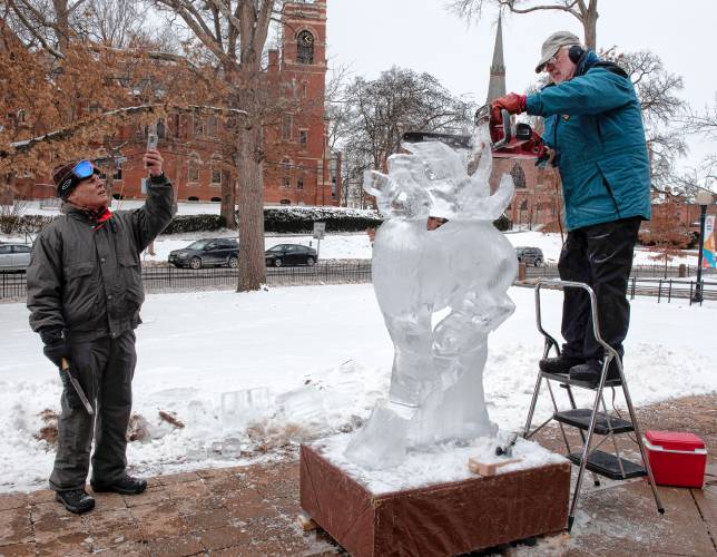 Jeff Zesiger, left, takes pictures while David Barclay works on an ice sculpture in front of Forbes Library for Winterfest. Zesiger is one of the participating artists on Saturday. 