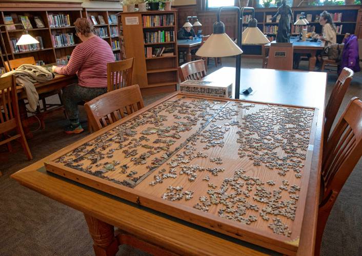A Puzzle sits on a table in the reading room which has newspapers, magazines,  new and old fiction with various tables and comfortable places to  sit. 