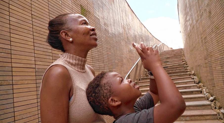 Tandiwe Njobe and her son, Nkosana, examine a memorial in South Africa to victims of apartheid in a scene from “Where I Became.” They’re looking for the name of Tandiwe Njobe’s brother.