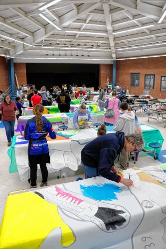 Bill Comeaux, front, works with dozens of community members to paint 52 panels to create a 1,500-square-foot mural for JFK Middle School during a community painting party Saturday afternoon in the school cafeteria.
